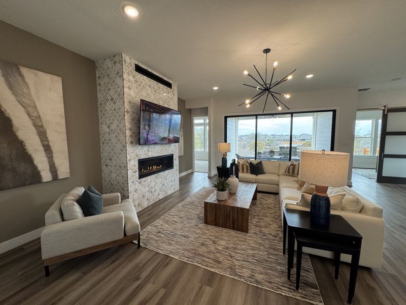 A modern living room featuring a sleek fireplace, stylish chandelier, and large windows with natural light and views.