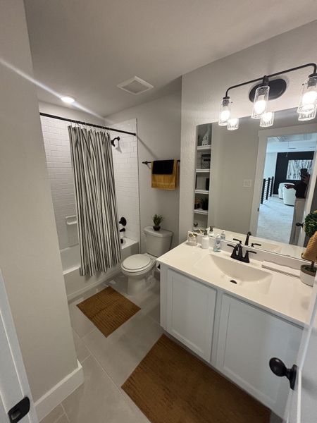 A stylish bathroom featuring a white vanity, black fixtures, and a subway-tiled bathtub with a bold striped shower curtain. A stylish bathroom featuring a white vanity, black fixtures, and a subway-tiled bathtub with a bold striped shower curtain.