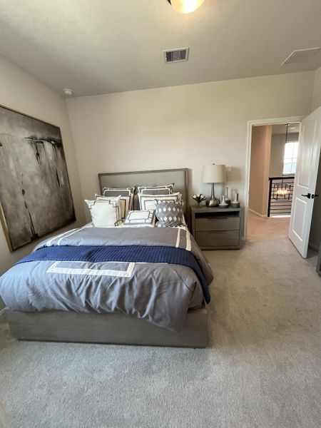 A cozy bedroom featuring a plush bed with layered bedding, modern artwork, and soft carpet flooring.