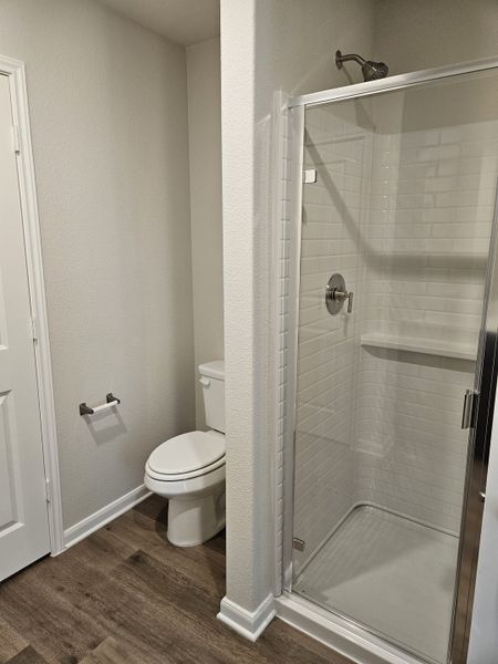 A sleek bathroom featuring a glass shower, white tiles, and wood-look flooring for a modern touch.