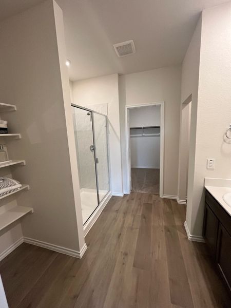 A modern bathroom featuring a sleek glass shower, spacious closet, chic shelving, and elegant wooden flooring.