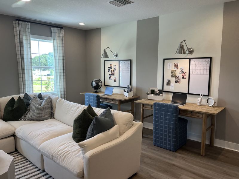 A cozy home office with dual desks, soft beige sofa, and large window, perfect for productivity and relaxation.