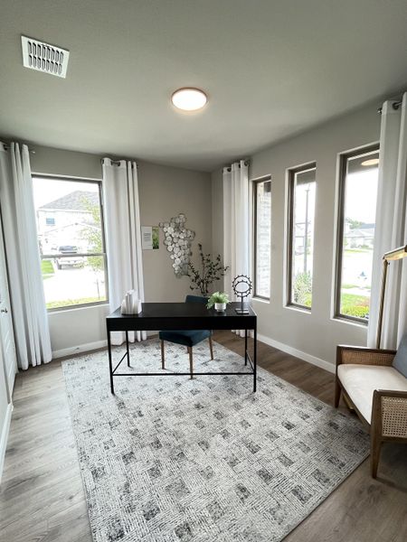 A bright home office with natural light, a sleek black desk, cozy seating, and elegant decor.