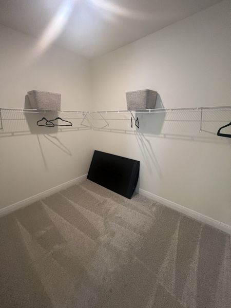 A spacious walk-in closet with white wire shelving, soft carpet, and ample storage bins. A spacious walk-in closet with white wire shelving, soft carpet, and ample storage bins.