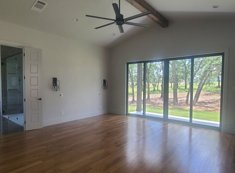 A bright room with hardwood floors, a ceiling fan, and large sliding doors opening to a serene wooded view.