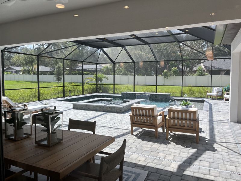 A spacious screened-in patio with a dining area, pool, and hot tub, perfect for relaxing and entertaining.