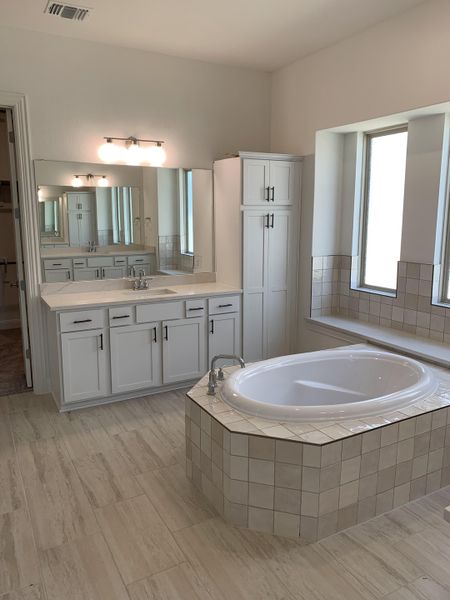 A spacious bathroom featuring a tiled bathtub, double vanity with mirrors, and ample natural light. A spacious bathroom featuring a tiled bathtub, double vanity with mirrors, and ample natural light.