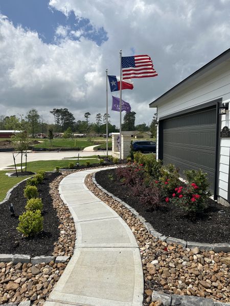 A charming home with a landscaped walkway and flags in Maple Heights by Century Communities (Porter Heights, TX).