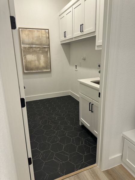 A sleek laundry room with hexagonal black tile flooring, white cabinets, and modern artwork. A sleek laundry room with hexagonal black tile flooring, white cabinets, and modern artwork.