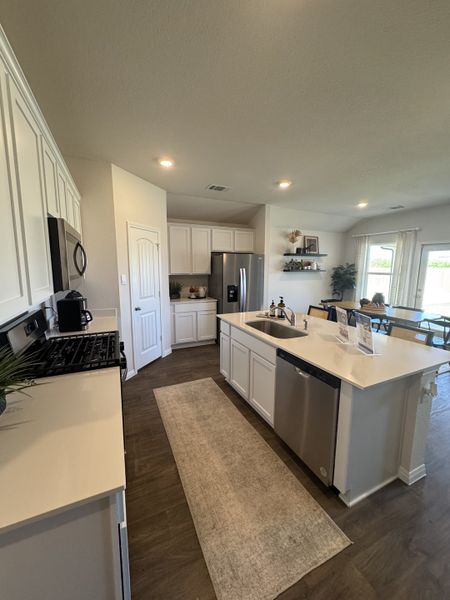 A modern kitchen with white cabinetry, stainless appliances, and sleek countertops, accented by dark wood flooring.