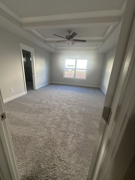 A spacious bedroom with plush carpet, elegant tray ceiling, and a large window for natural light. A spacious bedroom with plush carpet, elegant tray ceiling, and a large window for natural light.