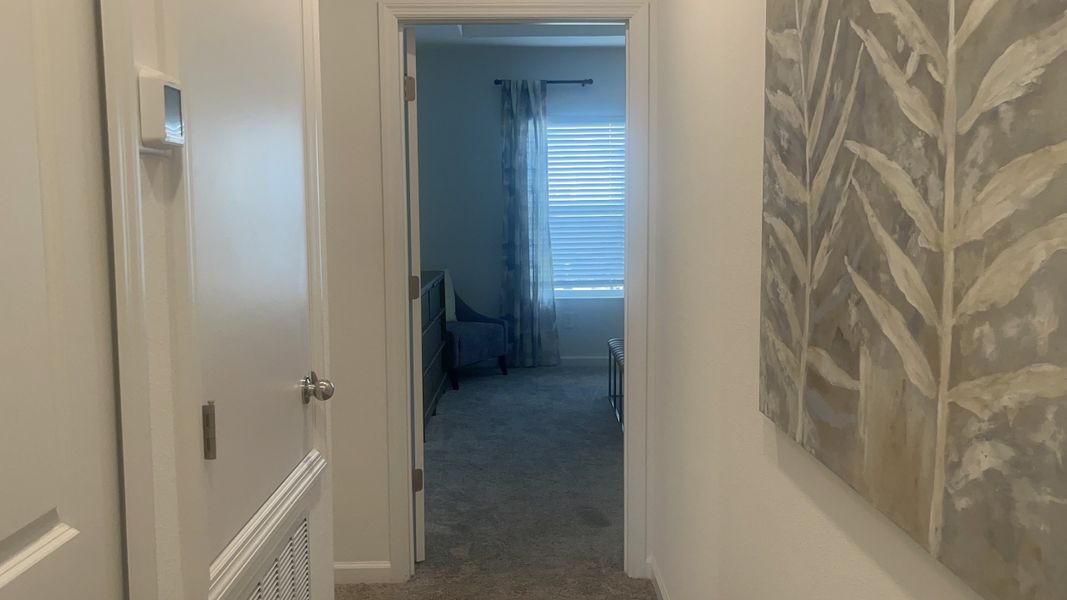 A cozy hallway leading to a bright room with neutral tones and modern decor. Featuring carpeted flooring and soft light.