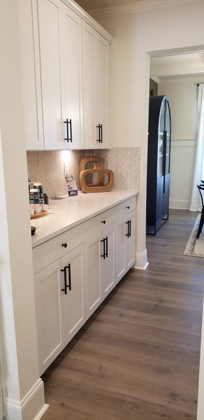 A modern kitchen nook with sleek white cabinetry, a herringbone backsplash, and elegant black hardware.