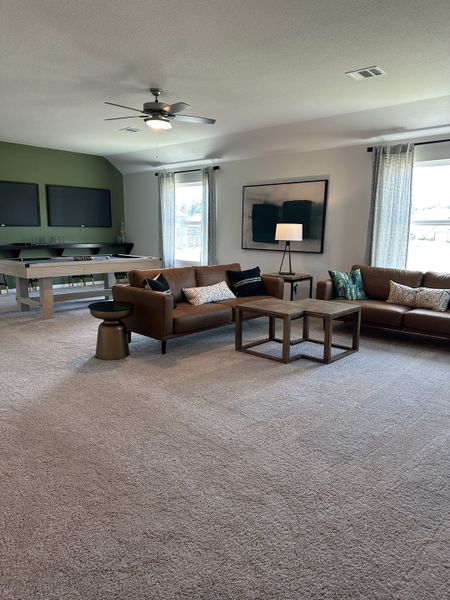 A spacious living room with brown sofas, a pool table, and modern decor, featuring neutral tones and abundant natural light.