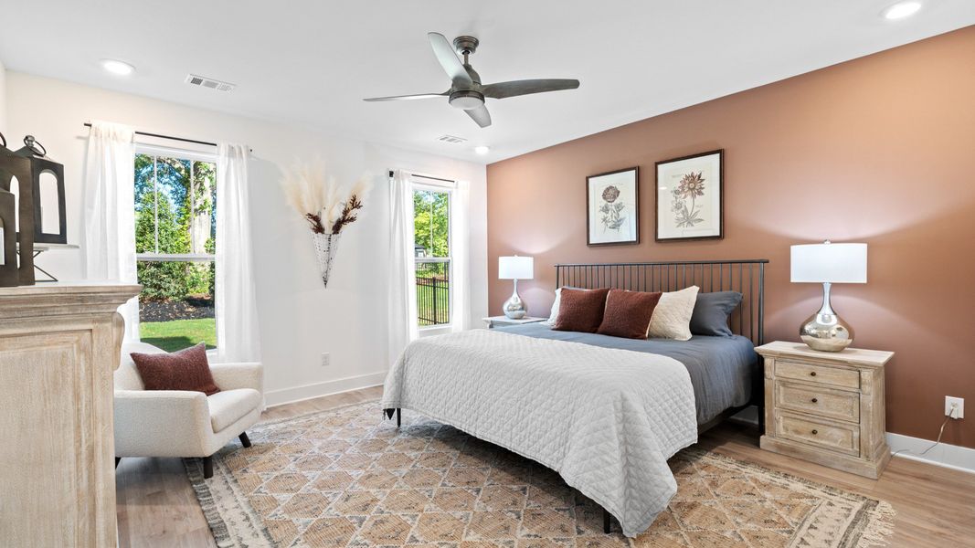 Cozy, inviting primary suite with floor to ceiling windows, ceiling fan, and hardwood flooring at Iris Meadows by DRB Homes