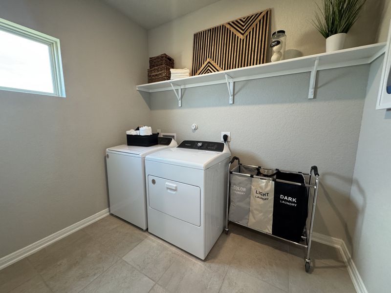 A well-organized laundry room featuring a washer, dryer, shelving, and sleek hampers.