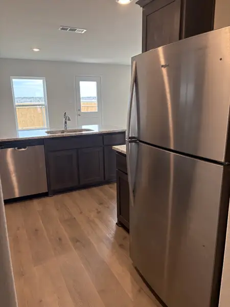 A contemporary kitchen featuring sleek stainless steel appliances, wood flooring, and large windows for ample natural light.