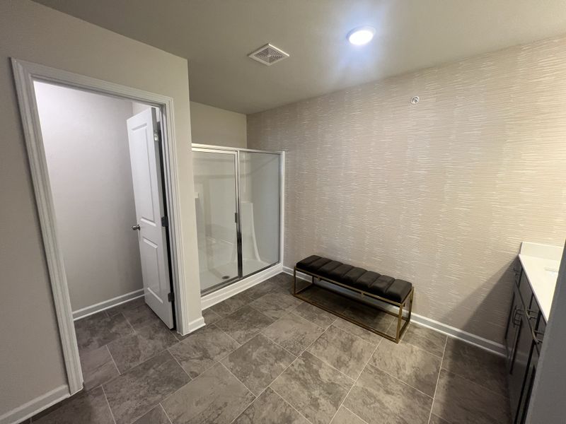 A spacious bathroom with sleek tile flooring, a glass shower, elegant bench, and modern vanity.