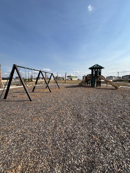 A vibrant children’s playground with swings, slides, and a mulch-covered play area, designed for outdoor fun in Crossroads at Kelly Park by Dream Finders Homes (Apopka, FL).