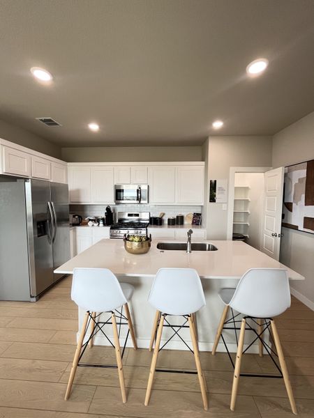 A modern kitchen with white cabinetry, sleek appliances, and a central island with stylish barstools.