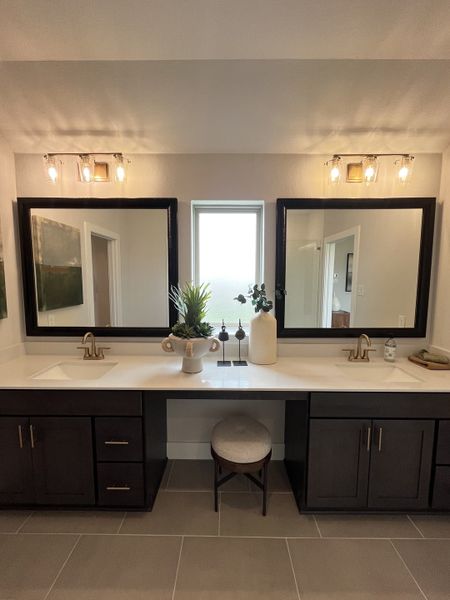 A modern bathroom featuring dual sinks, elegant mirrors, dark cabinetry, and stylish lighting.