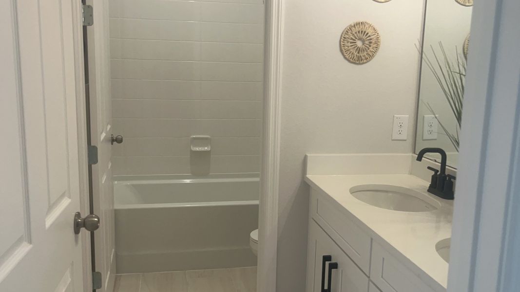 Modern bathroom featuring a sleek bathtub, white vanity, black fixtures, and decorative wall accents.
