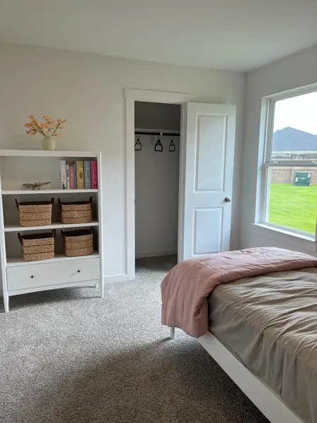 A cozy bedroom with a soft pink bedding, plush carpet, white shelving unit, and an inviting closet space.