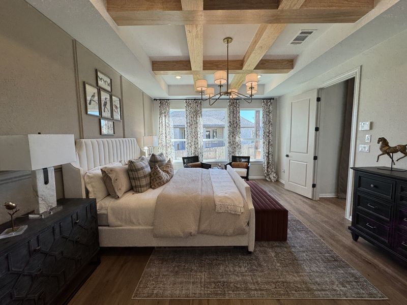 A cozy bedroom with a tufted bed, wooden beam ceiling, and elegant lighting, featuring stylish wall art and patterned curtains.