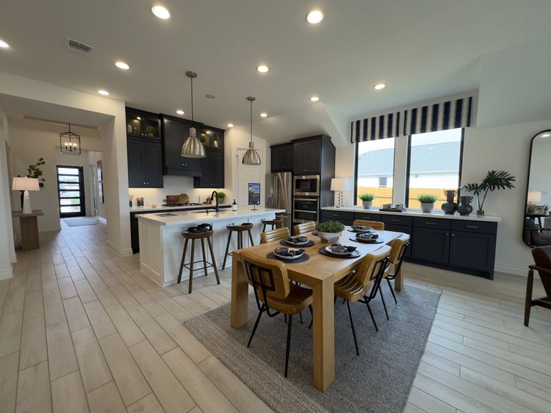 A modern kitchen and dining area with sleek black cabinets, pendant lighting, and a wooden dining table set for four.