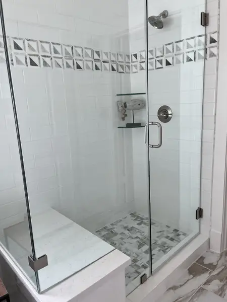 A modern shower with geometric tile accents, glass doors, and sleek fixtures in a stylish bathroom.