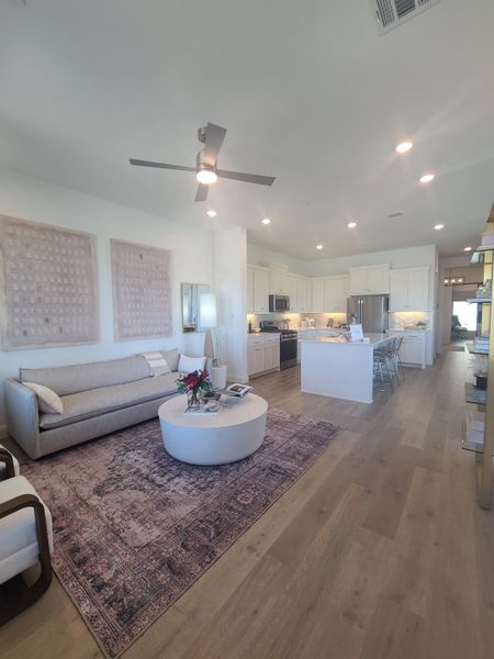 A spacious living area with a sleek ceiling fan, modern furniture, and an inviting open kitchen layout.