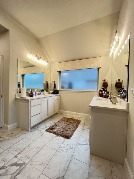 A spacious bathroom featuring marble floors, dual vanities, and elegant lighting, complemented by a large frosted window.