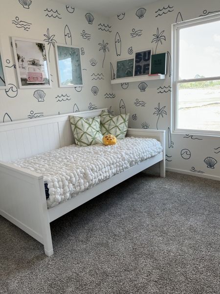 A coastal-themed bedroom with nautical wallpaper, a cozy white daybed, and decorative pillows creates a relaxing retreat.