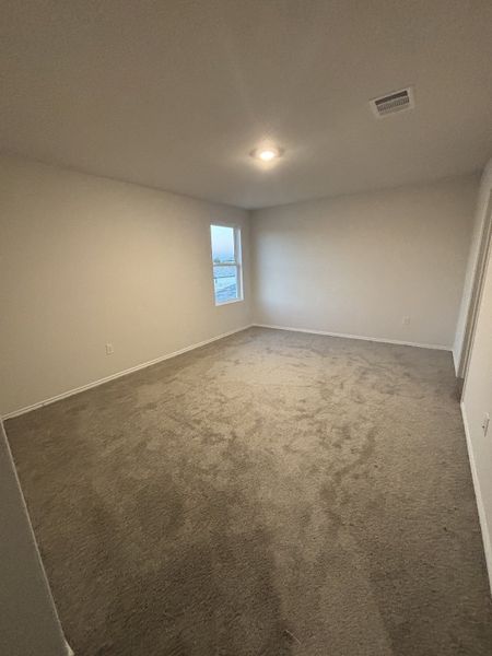 A spacious bedroom with soft carpet, a large window, and neutral walls for a cozy atmosphere.