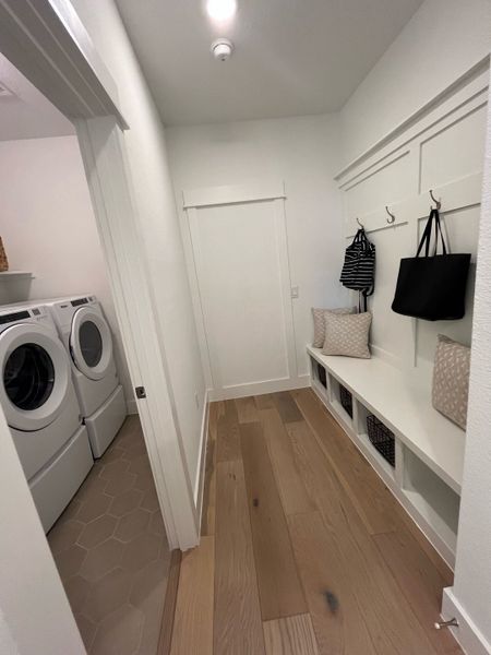 A functional laundry room with hardwood floors, built-in storage, and a sleek washer and dryer setup.