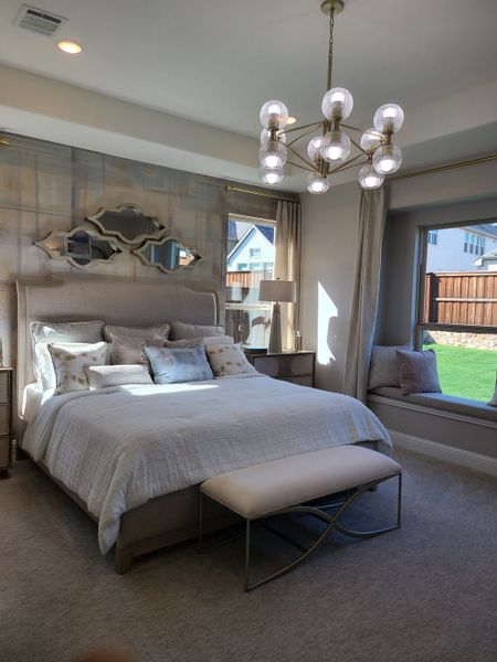 A cozy bedroom with a plush bed, elegant chandelier, and a sunny window seat.