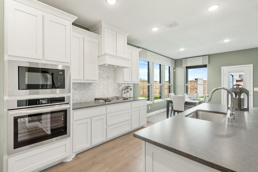 Kitchen with white cabinets, gray countertops, stainless steel appliances, and marble tile backsplash