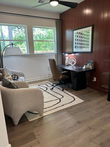 A cozy home office with a textured accent wall, sleek desk, modern chair, and large windows overlooking greenery.