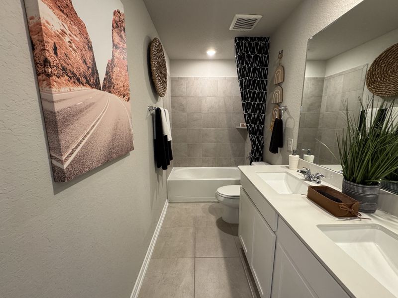 A modern bathroom featuring dual sinks, neutral tones, abstract decor, and a tiled bathtub area.