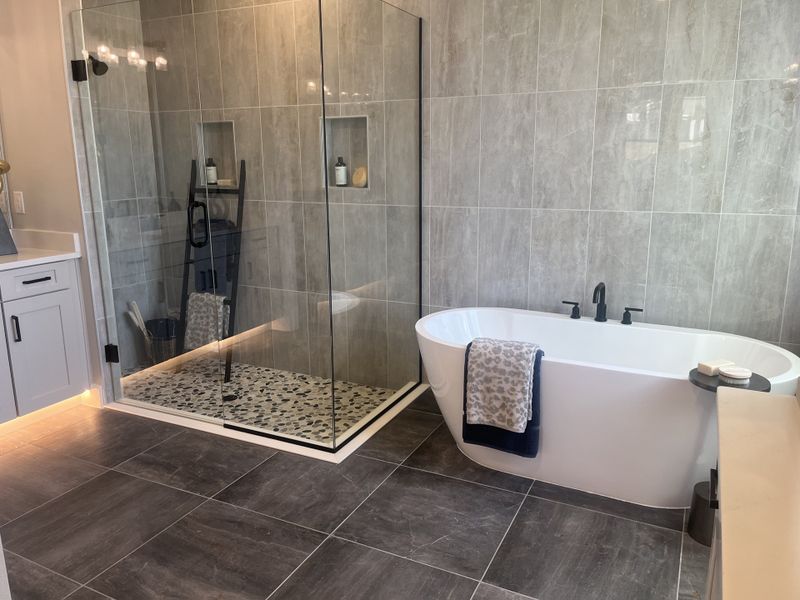 A luxurious bathroom featuring a spacious glass shower, a sleek standalone tub, and elegant gray tiling. A luxurious bathroom featuring a spacious glass shower, a sleek standalone tub, and elegant gray tiling.