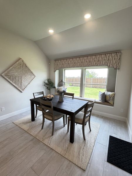 A cozy dining area with a dark wood table, modern chairs, large window seat, and soft lighting.