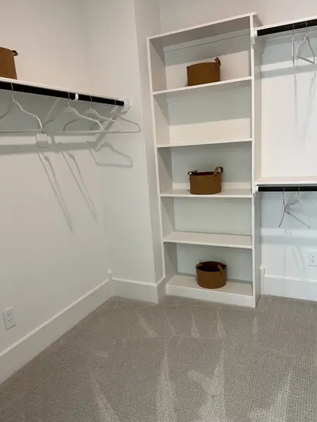 A spacious walk-in closet with carpeted flooring, open shelving, and hanging rods for ample storage.