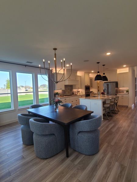 A modern dining area with plush chairs, a sleek dark table, and an open kitchen illuminated by elegant lighting.