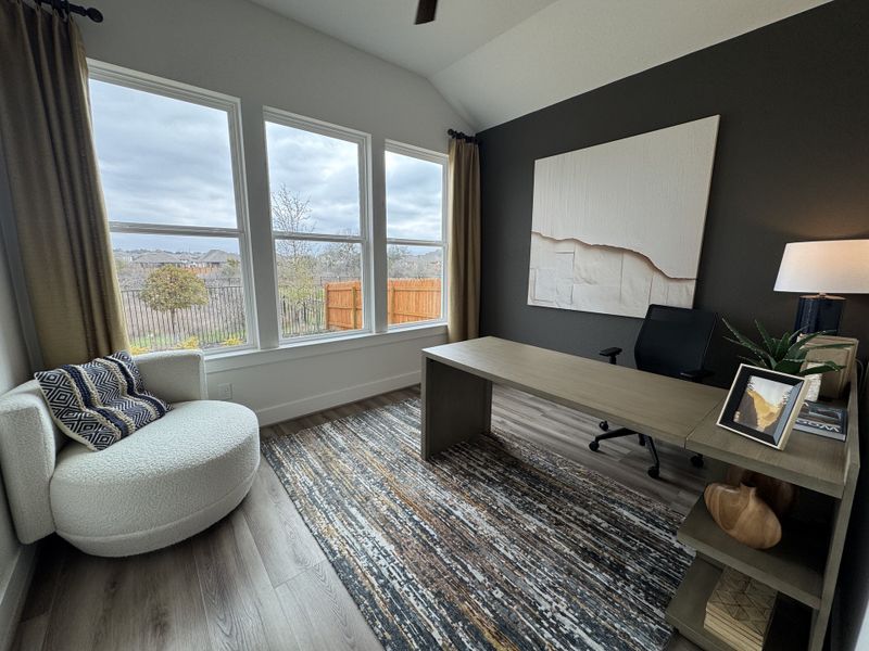 A modern home office with a large window, sleek desk, cozy armchair, and abstract wall art.