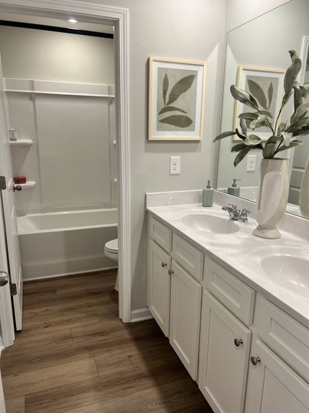 A modern bathroom featuring a sleek vanity, double sinks, and elegant decor with wood flooring.