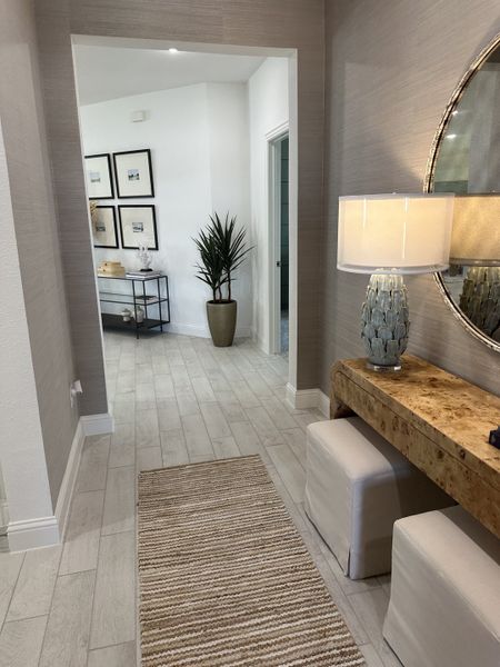 A chic hallway with light wood flooring, elegant decor, a textured rug, and stylish lighting. A chic hallway with light wood flooring, elegant decor, a textured rug, and stylish lighting.
