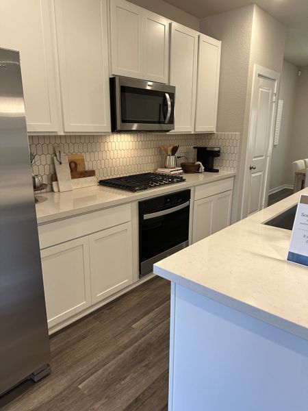 A sleek kitchen with white cabinets, a stainless steel microwave, and a hexagon-tiled backsplash.