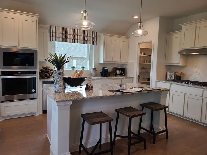 A modern kitchen with granite countertops, a spacious island, pendant lighting, and sleek white cabinetry. A modern kitchen with granite countertops, a spacious island, pendant lighting, and sleek white cabinetry.