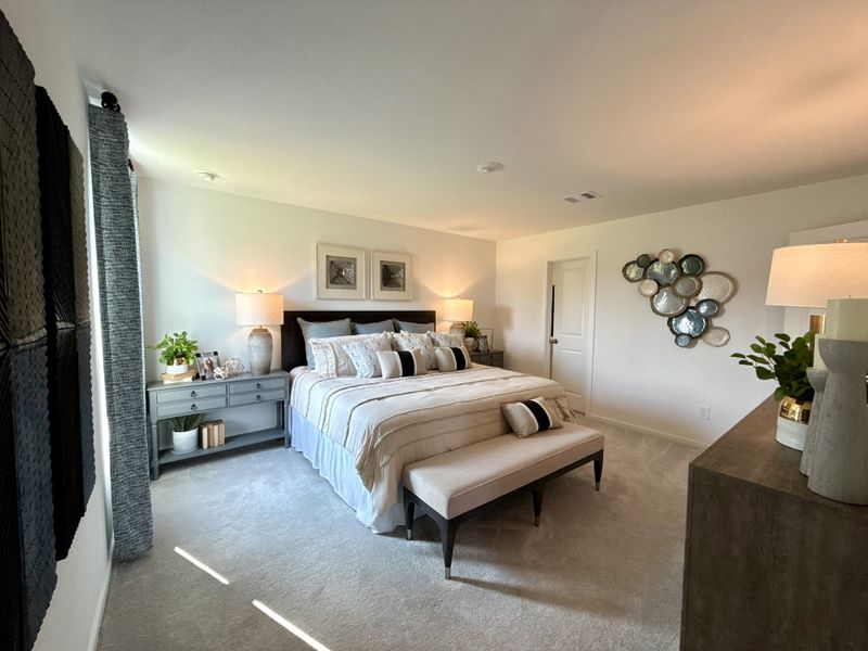 A cozy bedroom featuring soft bedding, a stylish bench, elegant lighting, and decorative wall art.