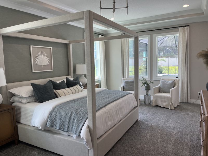A cozy bedroom featuring a stylish canopy bed, soft gray accents, and ample natural light from large windows.